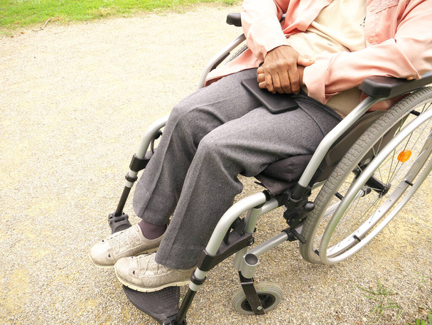 Közelkép egy tolószékes, idős, fogyatékos fekete nő holttestéről, aki a lábán tartja a telefonját. - Fotó, kép