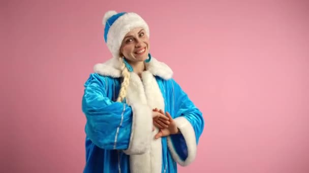 Hezká usměvavá žena v modrém kostýmu Sněhurky v modrém klobouku s bílou kožešinou a dlouhým copem, šťastná Santa žena tančící na růžovém pozadí, příprava na zimní vánoční představení - Záběry, video