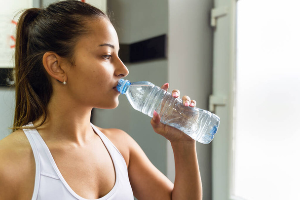 Side view close up on young adult caucasian female drinking water at gym in day - copy space - Foto, afbeelding
