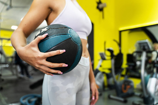 Nahaufnahme einer unbekannten kaukasischen Frau mit Medizinball im Fitnessstudio, die mitten im Training steht - Gesundheits- und Fitnesskonzept - Foto, Bild