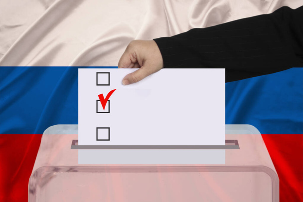 Wählerin senkt den Stimmzettel in einer transparenten Wahlurne vor dem Hintergrund der russischen Nationalflagge Konzept der staatlichen Wahlen, Referendum - Foto, Bild
