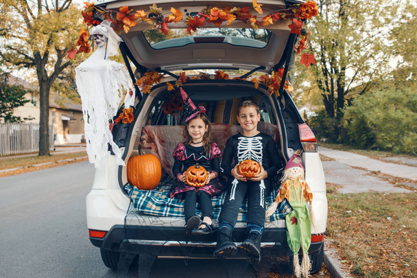 トリックやトランク.兄弟姉妹は車のトランクでハロウィンを祝う。10月の休日の屋外を祝う子供の男の子と女の子。社会的距離と安全な代替お祝い. - 写真・画像