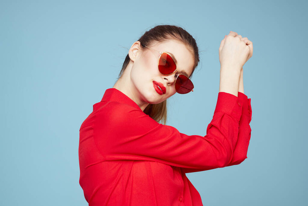 Femme avec des lunettes sombres lèvres rouges charme chemise studio fond bleu - Photo, image
