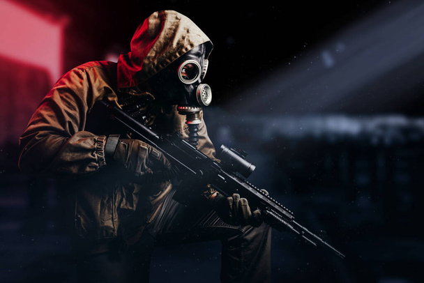 Photo of a post apocalyptic stalker soldier in gas mask and hood jacket holding rifle and sitting on dark factory background with red light glow. - Fotografie, Obrázek