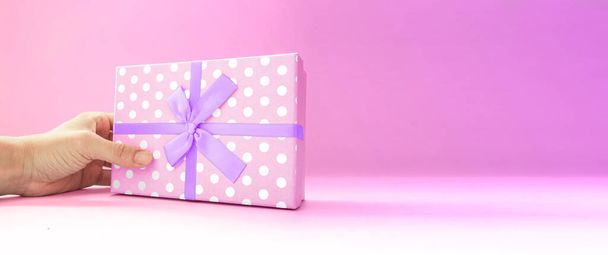 Человеческая рука с розовой подарочной коробкой, белой точечной оберточной бумагой, на глубоком розовом фоне, копировальное пространство, вид сбоку, на день отца, День матери, Рождество, день рождения. - Фото, изображение