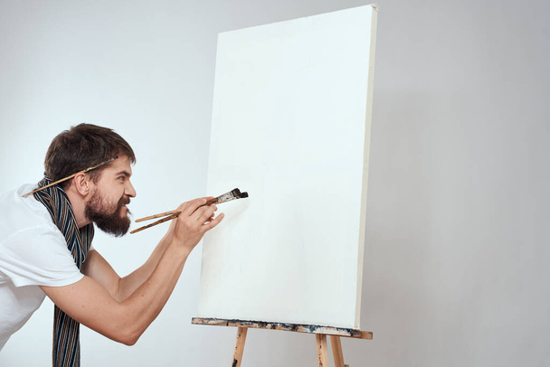 Muž umělec štětec v rukou stojan umění hobby světlo pozadí šála kolem krku - Fotografie, Obrázek