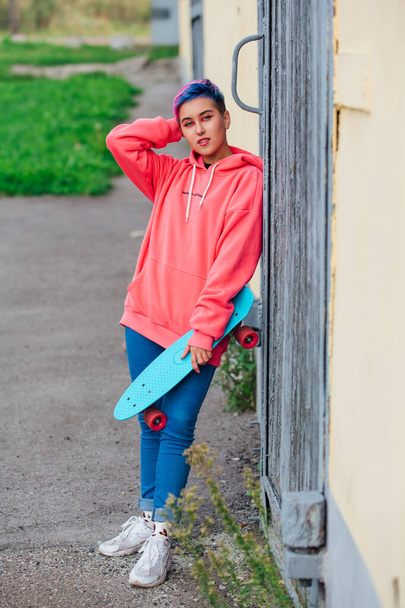 Stylish young woman with short colored hair holding blue plastic skateboard in hand. Youth concept. - Valokuva, kuva