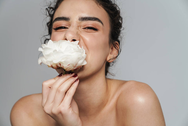 Image of pleased half-naked woman eating white flower on camera isolated over gray wall - Foto, imagen