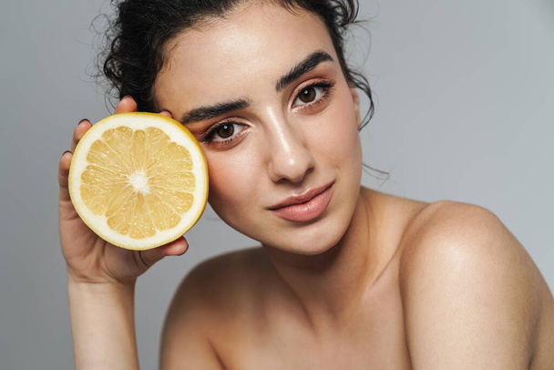 Image of seductive half-naked woman looking at camera while posing with lemon isolated over gray wall - Фото, зображення