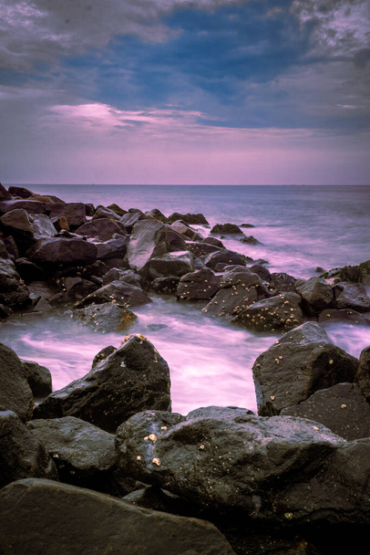 Prachtige zonsopgang over het strand in lange blootstelling. Bewegende elementen zonsopgang en golffotografie vanaf het rotsachtige strand in India. Wave breaker rotsen, slow-shutter Sea Waves en Rocks fotografie. - Foto, afbeelding