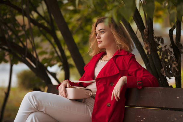 Elegant woman in red coat sitting on a bench in autumn park - Foto, Bild