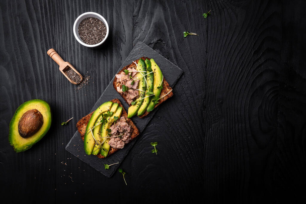 Sandwiches with avocado and tuna fish, microgreen. Toasts with tuna delicious healthy food on a dark background, Top view, flat lay. - Foto, immagini