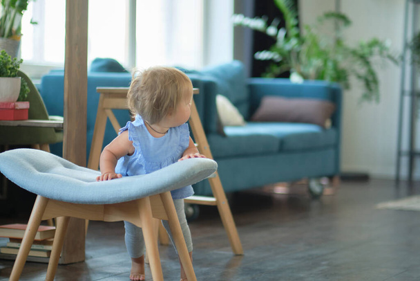 A menina de olhos azuis aprende a andar agarrando-se à cadeira. rosto de bebê feliz - Foto, Imagem