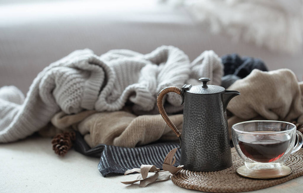 Glass cup of tea with a teapot on the background of warm clothes in cold colors. Autumn composition - Foto, Imagem