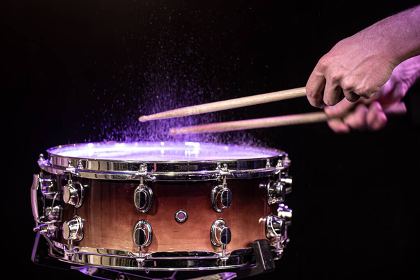 Drumsticks raken snare drum met spetterend water op zwarte achtergrond onder studioverlichting close-up. - Foto, afbeelding