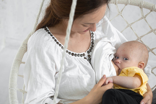 Feliz mamá alimenta al bebé en una hamaca blanca sobre un fondo blanco de cerca. Concepto de maternidad feliz. - Foto, Imagen