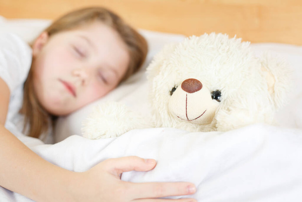 girl is sleeping with a soft toy on white bed - Foto, imagen