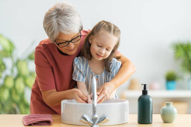 A cute little girl and her grandmother are washing their hands. Protection against infections and viruses.   - Фото, изображение
