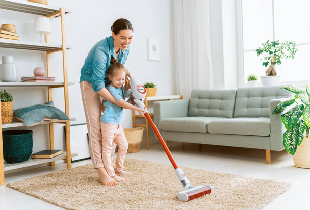 Happy family vacuuming the room. Mother and daughter doing the cleaning in the house. - Foto, imagen