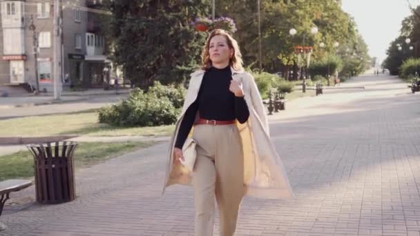Stílusos fiatal nő sétál végig a város utcáján egy fényes, napos napon. Divatos modern ruhák egy üzletasszonyon. A személy magabiztos magában.. - Felvétel, videó