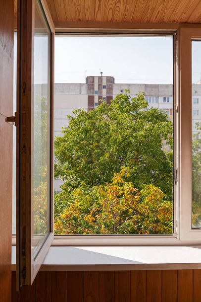Nyitott ablak és a fa belsejének egy része, az őszi többszintes épület homályos hátterén, diófák ablakán keresztül. - Fotó, kép