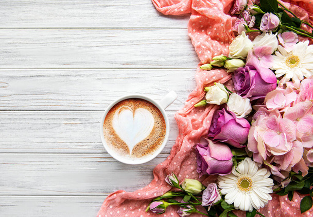 Flores rosadas y una taza de café sobre un fondo de madera blanca - Foto, Imagen