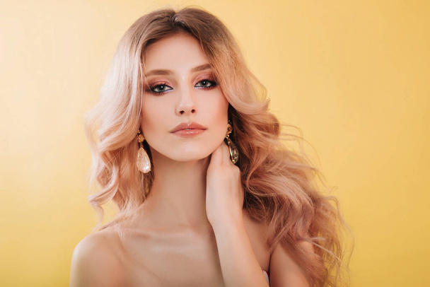 Beautiful, young model blonde close-up portrait. Girl with professional makeup and hairstyle, studio photo on a yellow background. Fashion photography - Foto, afbeelding