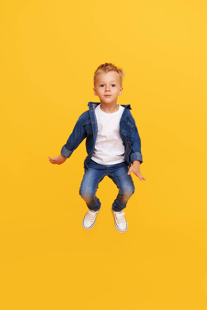Full length portrait of excited little child boy Jumping for joy isolated on yellow background. - Fotó, kép