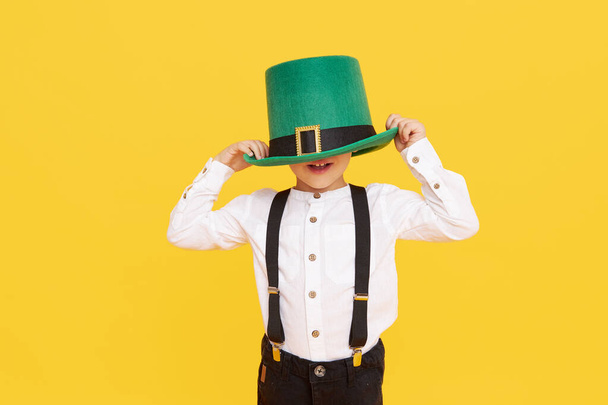 Smiling little child boy in green leprechaun hat on yellow background. St. Patrick Day celebration. Funny face - Fotó, kép