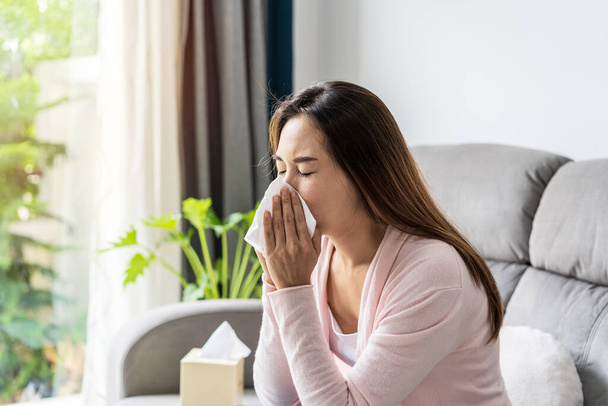 Young asian women with allergies feeling unwell using tissues and sneezing at home - Фото, изображение