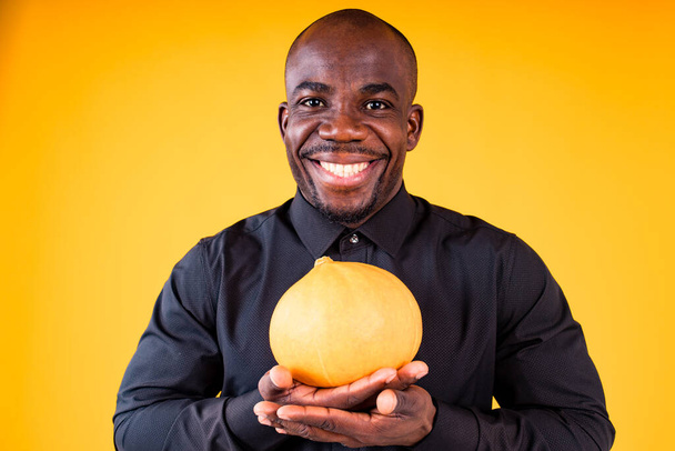 People and Halloween preparation concept, man holding small pumpkin in studio yellow background - Photo, image
