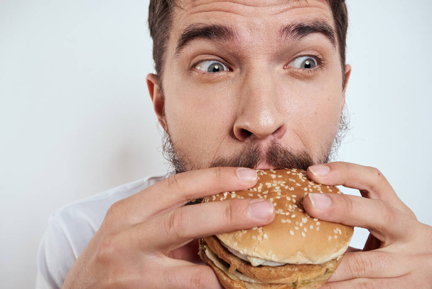 白いTシャツに身を包んだ男がハンバーガーを食べると、空腹のファーストフードが近くに見える - 写真・画像