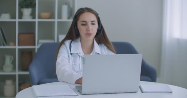 Nainen lääkintäavustaja pukeutuu valkoiseen takkiin, kuulokkeet video soittaa etäinen potilas kannettavan. Lääkäri puhuu asiakkaalle virtuaalisen chat tietokone sovellus. Telelääketiede, etäterveydenhuollon palvelukonsepti. - Materiaali, video