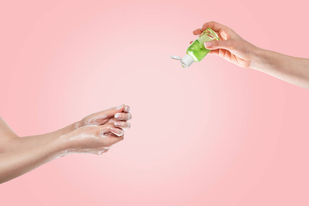 Dezenfeksiyon ve bakteri ve virüslerden korunma kavramı. Kadınların elleri altta sabunla, kadınların elleri üstte antibakteriyel jelle yıkanır. Eller yakın plan. Pembe arka plan.. - Fotoğraf, Görsel