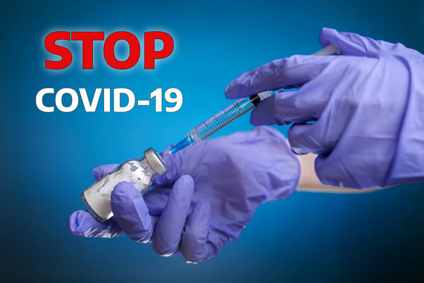 Schluss mit COVID-19. Die Hand eines Arztes oder Wissenschaftlers in medizinischen Handschuhen hält eine Flasche und füllt eine Spritze mit Medikamenten. Blauer Hintergrund. Das Konzept von Coronavirus, Impfstoffen und Gesundheit. - Foto, Bild