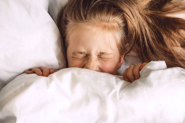 Kind versteckt sich unter Bettdecke im Bett - Foto, Bild