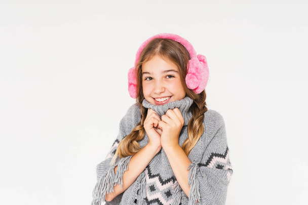 Cute smiling teenage girl in pink fur headphones and gray poncho looks up isolated on white background - Photo, Image