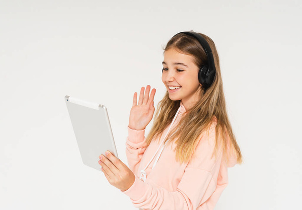 Söpö hymyilevä teini tyttö kuulokkeet ja tabletti käsissään eristetty valkoisella taustalla, videopuhelu - Valokuva, kuva