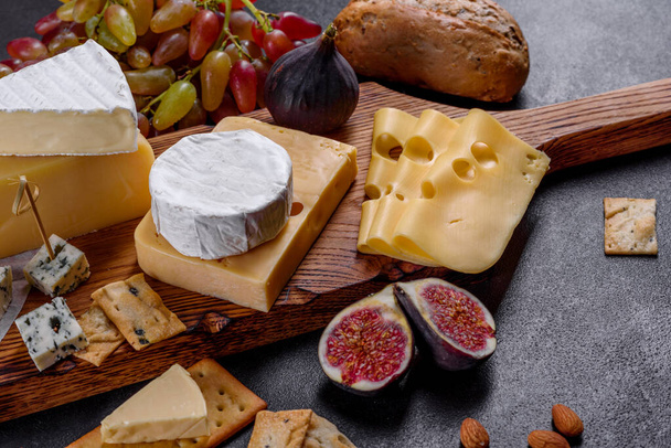 Όμορφο νόστιμο τυρί καμαμπέρ, παρμεζάνα, μπρι με σταφύλια και σύκα σε ξύλινη σανίδα. Σνακ για κρασί στις διακοπές - Φωτογραφία, εικόνα