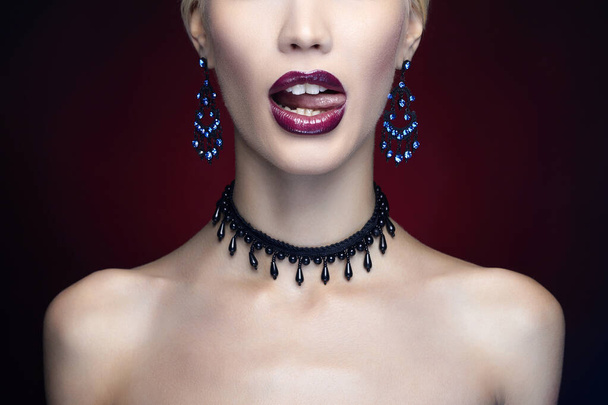 Beautiful girl licking the tongue with shiny lips. Art make-up young woman in necklace - Фото, изображение