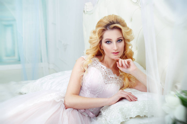 Portrait of a beautiful blonde bride with elegant curls on the bed in the boudoir. - Zdjęcie, obraz