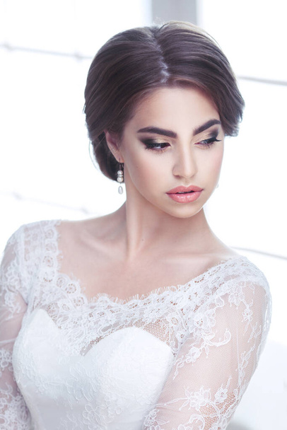 Portrait of a beautiful bright brunette bride with downcast eyes in lace dress - Fotó, kép