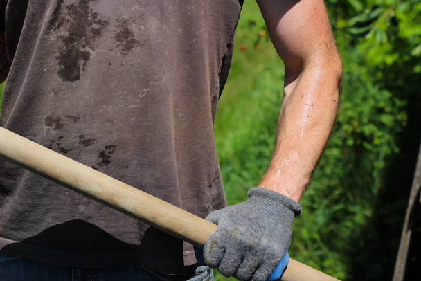 Obrero sucio sostiene una pala en sus manos bajo el sol abrasador - Foto, Imagen