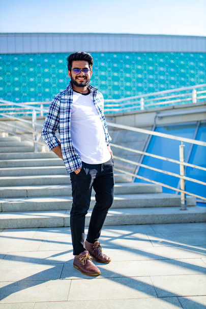 arabian young man in stylish checkered shirt and white t-shirt in downtown at summer day - Foto, Imagen