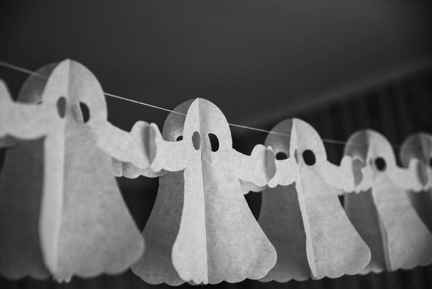 Halloween decorarion. Concept DIY and children creativity. Step-by-step instructions: making garland of ghosts from white and black paper. Step 3 child throughout rope from paper ghost - Photo, Image