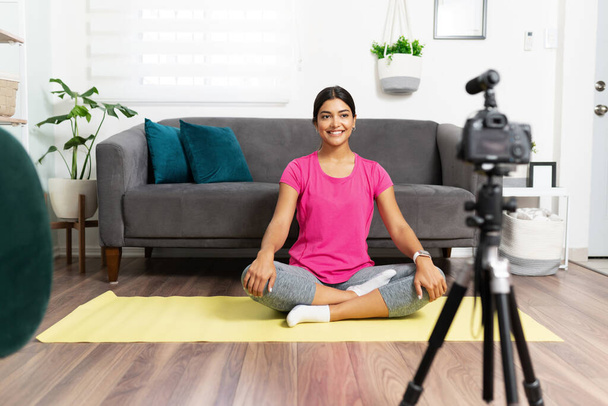 Портрет прекрасного латиноамериканського тренера, який сидить на йога маті і готовий записати відео для своєї онлайн-аудиторії з дому. - Фото, зображення