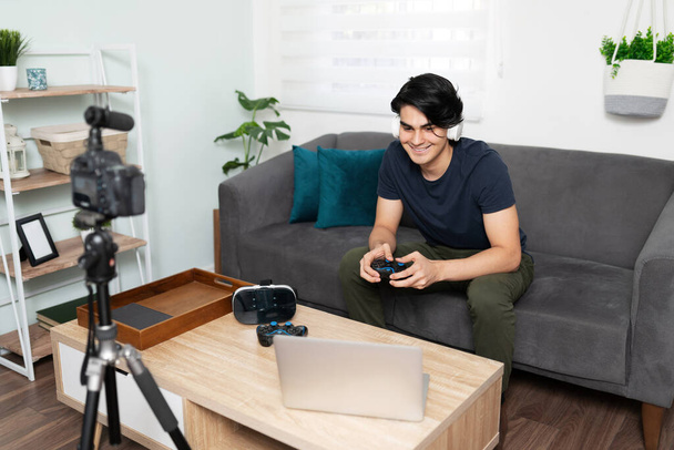 Portrait d'un jeune homme attrayant et blogueur jouant à des jeux vidéo et les examinant pour ses disciples en ligne - Photo, image