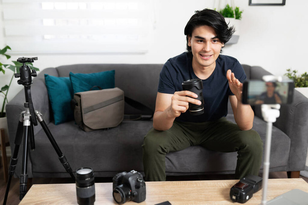 Jeune homme et blogueur vidéo examinant certains équipements de photographie et parlant d'un nouvel objectif qu'il vient de recevoir à son public des médias sociaux - Photo, image