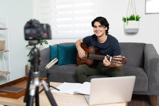 İspanyol asıllı müzisyen ve müzisyenin portresi gitar çalarken ve takipçileri için şarkı söylerken bir video kaydediyor. - Fotoğraf, Görsel