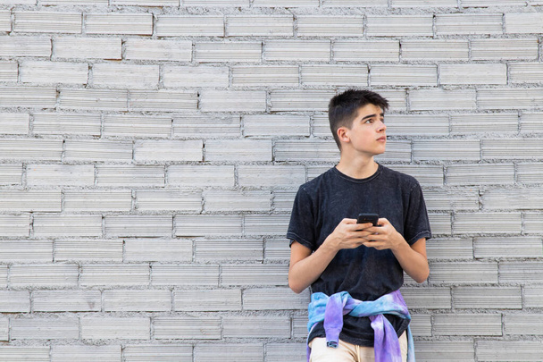 teenager boy with mobile phone on the wall of the city street outdoors - Fotoğraf, Görsel